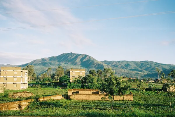 Buildings and fields in Mbeya with green hills behind.