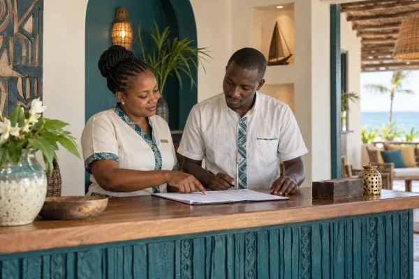 Editorial illustration: Two hotel staff reviewing a document at reception.